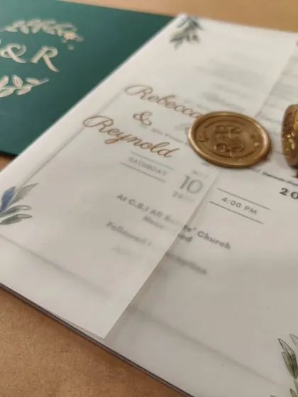 A bespoke wedding invitation with a printed vellum jacket, sealed with a gold wax seal and paired with a deep green envelope.