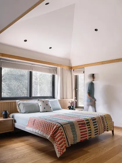 This master bedroom in Cocoon House features a high, pitched ceiling that enhances the sense of space and tranquility. We kept the design minimal with a low-profile bed, natural wood flooring, and a colorful handwoven bedspread that adds a layer of texture and personality.