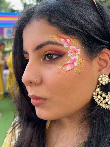 Floral designs are always in demand. This look combines delicate pink flowers with a sprinkle of gold glitter, perfect for a daytime event or a mehndi function. It's a beautiful example of how face art can complement a traditional look.