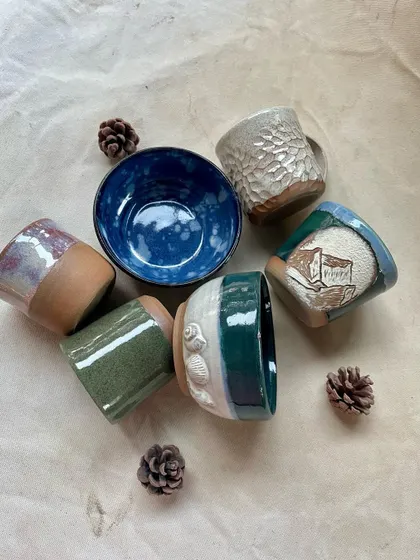 A collection of student-made mugs and bowls, showcasing a variety of textures and glaze combinations.