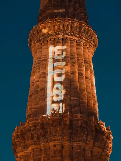 A close-up of the Qutub Minar at night, with projections lighting up its surface. This shot showcases the monument in a modern light, highlighting its intricate details.