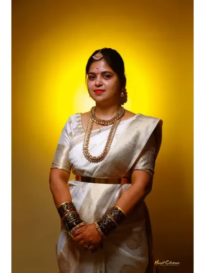 A striking portrait of the bride in a white silk saree, set against a warm yellow background that makes her attire pop.