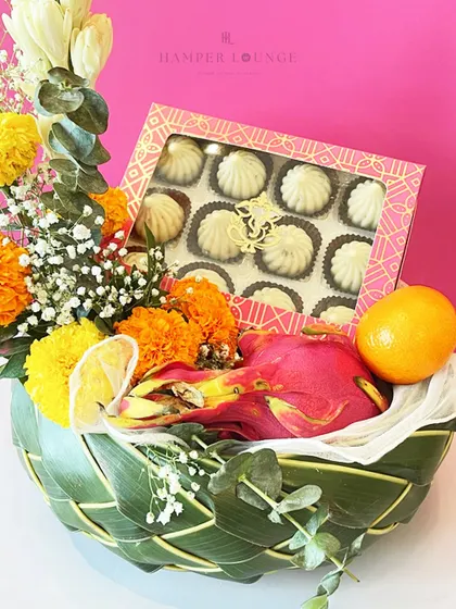 A detailed shot of the Ganesh Chaturthi hamper, focusing on the box of delicious modaks nestled among fresh marigolds and exotic fruits. It’s a perfect blend of tradition and freshness.