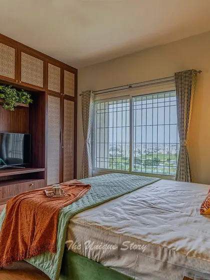 A master bedroom after its renovation, featuring beautiful wooden wardrobes with traditional cane webbing. The green upholstered bed and earthy orange throw create a warm, inviting, and subtly Indian contemporary look.