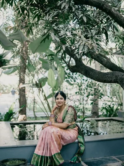 A stunning wide shot of the bride in a serene, natural setting. The makeup is designed to look beautiful from a distance, with enough definition to stand out.