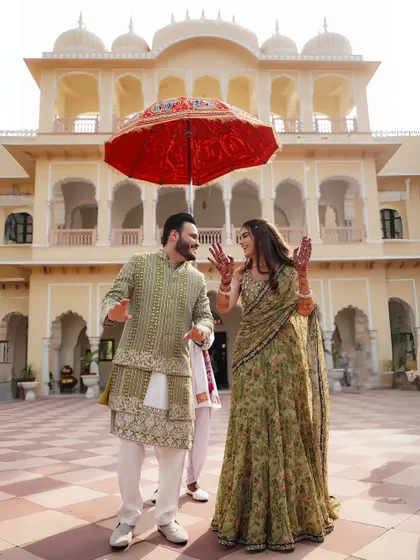 A playful moment during the Mehendi, with the couple dancing under a traditional Rajasthani umbrella, their joy evident.