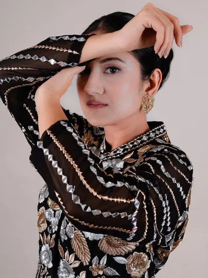 A striking beauty portrait where the model's hands frame her face, showcasing both her flawless makeup and the detailed sleeve of her outfit. This composition is both elegant and powerful.