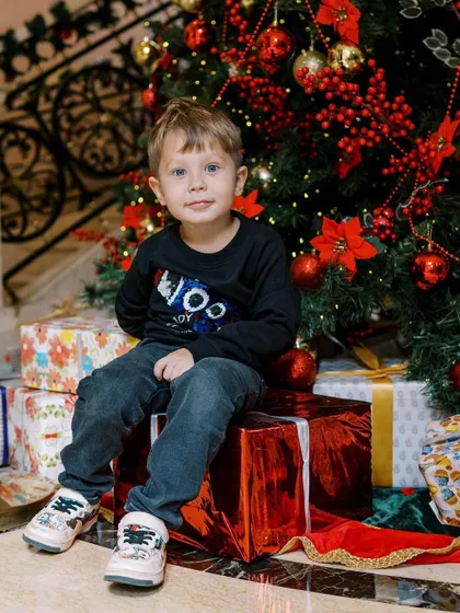 A handsome little boy sitting proudly by the Christmas tree. The vibrant colors and his sweet expression make this a perfect holiday photo.