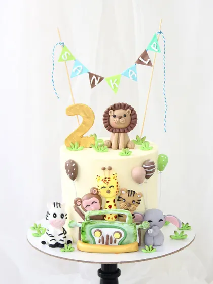 A delightful jungle safari cake perfect for a child's second birthday. This design is packed with fun, featuring adorable, handmade fondant animals like a lion, zebra, and monkey, all ready for a jeep adventure.