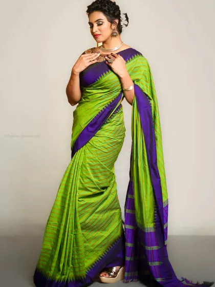 A full-length studio portrait in a vibrant green and purple saree. This is a classic look for showcasing traditional handloom sarees.