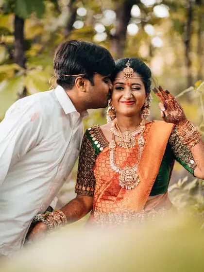 A sweet kiss on the cheek during a post-ceremony shoot in a natural setting, capturing the newlywed glow.
