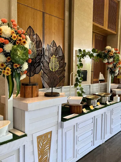 A clean and modern buffet station in white, accented with metal leaf sculptures and lush floral arrangements. This setup demonstrates our versatile design capabilities, suitable for any theme.