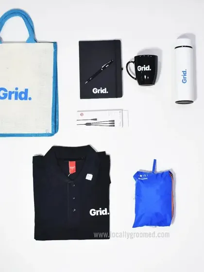 A comprehensive onboarding kit for Grid, featuring a branded polo shirt, a jute tote bag, a notebook and pen, a mug, a water bottle, and a rain poncho. This shows the variety of items we can source and brand for a complete welcome package.