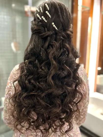 A half-updo with a braided crown and soft curls, accented with pearl pins. This is a classic and elegant choice for any wedding function.