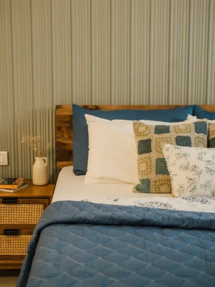 A close-up of a perfectly layered bed. This look combines a solid blue quilted coverlet, a crisp white pillow, and our custom cushion covers in complementary patterns and textures, creating a cozy and inviting sleep space.