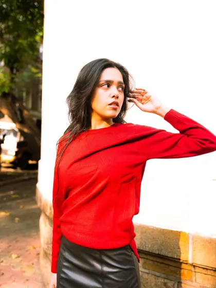 Using a simple white wall to make the bright red sweater pop. This is a great example of using color contrast in a portrait.
