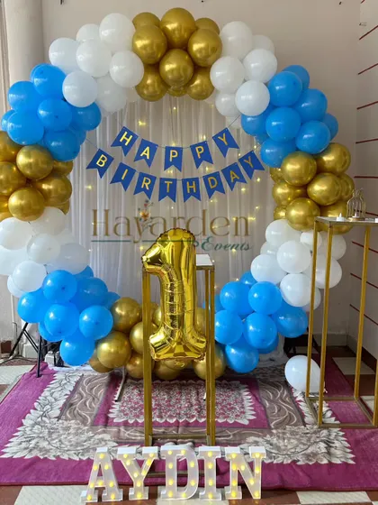 A classic blue, white, and gold first birthday party. The decor features a full balloon ring and a large gold foil number '1'.