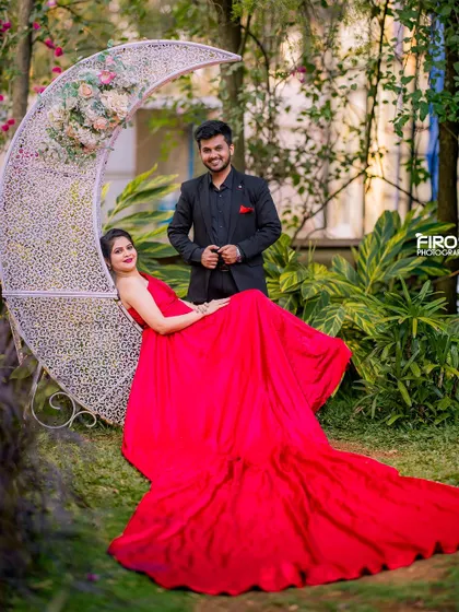 A beautiful portrait of a couple on a crescent moon seat, surrounded by a lush garden. The flowing red gown adds a touch of romance and drama to the scene.