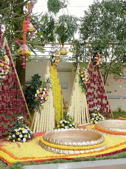 For this "Phoolon ki Haldi," we created a fun and festive backdrop using triangular frames. Two were filled with a weave of red and maroon flowers, while the center one was adorned with strings of bright yellow tuberoses.