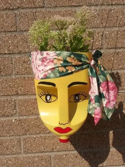 This stylish face planter, made from a yellow bottle and decorated with a floral bandana, adds a bohemian touch to a brick wall. It shows how recycled art can be chic and fashionable.