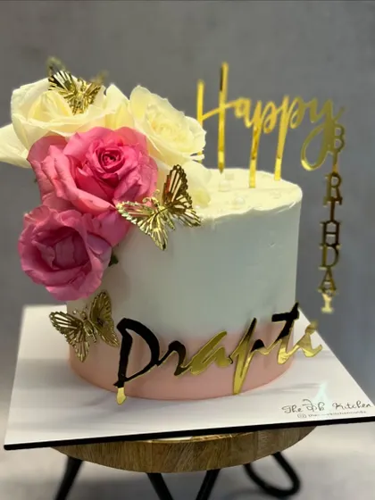 A simple yet elegant design with a two-tone pink and white buttercream finish. The cake is adorned with fresh roses, golden butterflies, and a custom nameplate.
