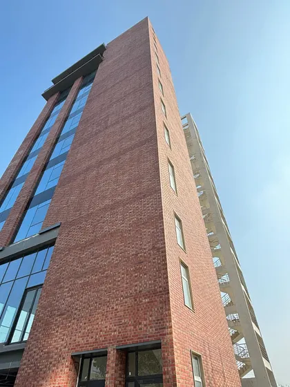 Looking up at the facade of a nearly completed office tower, this view shows the clean lines where the brickwork meets the sky. The adjacent concrete service core provides a neutral backdrop, highlighting the warmth of the primary material.