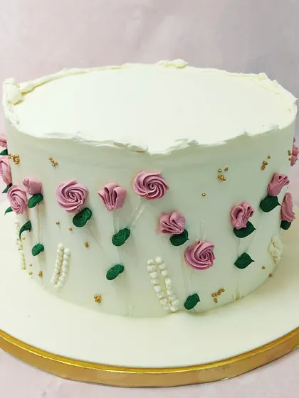We believe in the timeless beauty of simplicity with this elegant floral cake. A pristine white buttercream canvas is adorned with delicate, hand-piped pink rosebuds and tiny pearls, creating a classic and graceful design perfect for Mother's Day or an anniversary.