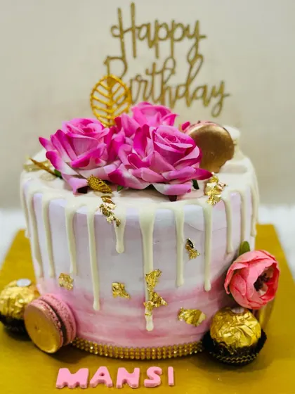 A pretty pink and white drip cake topped with vibrant pink roses and surrounded by macarons and Ferrero Rocher.