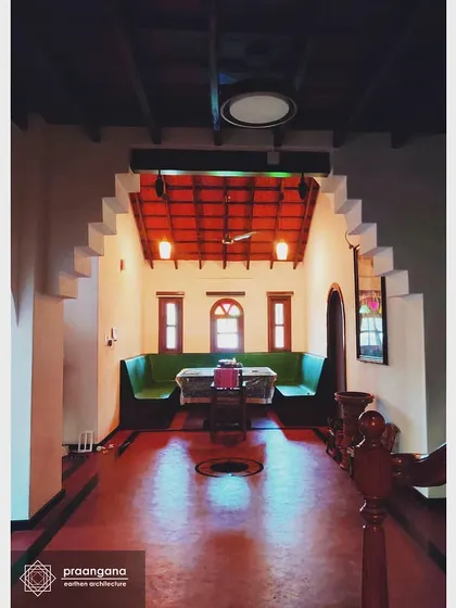 This is the heart of our Udupi residence project, a space that flows under a corbelled arch. The glossy red oxide floor reflects the light, contrasting beautifully with the cool white lime-plastered walls and the warm tones of the wooden ceiling beams.