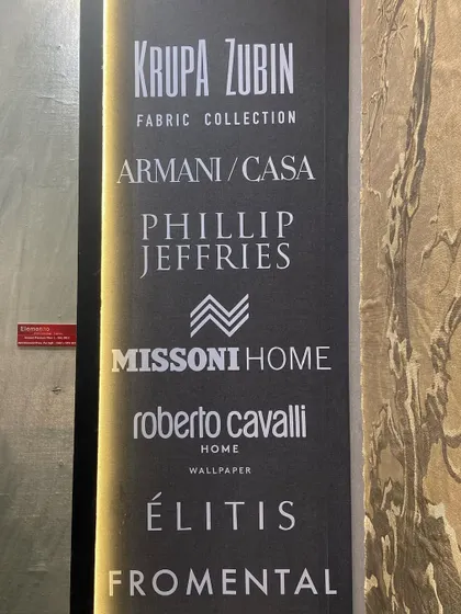 A sign at our booth listing some of the iconic brands we carry, including Armani Casa, Phillip Jeffries, Missoni Home, and Élitis. We are proud to be curators of the world's finest wallcoverings.