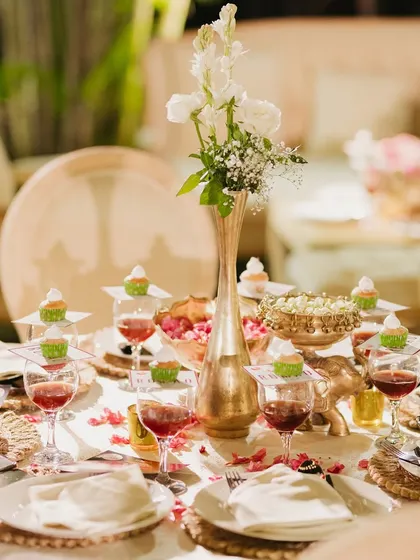 A beautifully set table at an elegant anniversary party. We used gold-rimmed plates, brass vases, and custom cupcakes on each wine glass to create a luxurious and personalized dining experience.