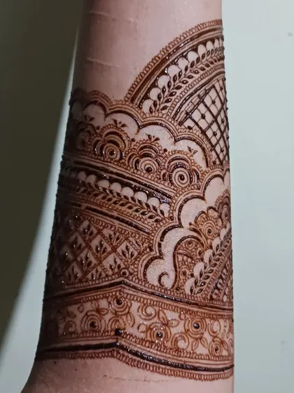A detailed shot of an intricate henna band on the forearm. This design uses layers of patterns, including swirls and grids, to create a rich texture.