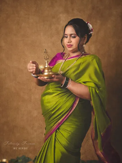 An expectant mother in a vibrant green and pink saree holds a brass diya. This traditional maternity portrait is rich in color and cultural details, celebrating the beauty of motherhood.