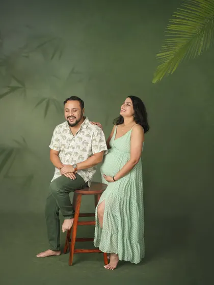 A candid moment of shared laughter between parents-to-be. This photo, taken against a nature-themed studio backdrop, captures the genuine joy and fun of their pregnancy journey.