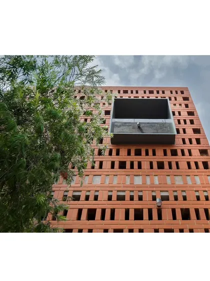 A detail of the brick facade, showing the 'jaali' or screen work. A metal box window projects out from the screen, creating a small balcony for the kid's bedroom and adding a modern, industrial element to the traditional brickwork.