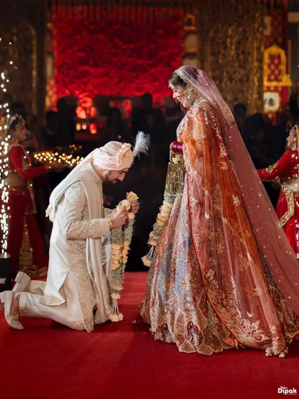 The groom bows in a gesture of reverence during the Jaimala ceremony. This moment, captured on a grand red carpeted stage, is a beautiful display of tradition and mutual respect, marking the official start of their life together.