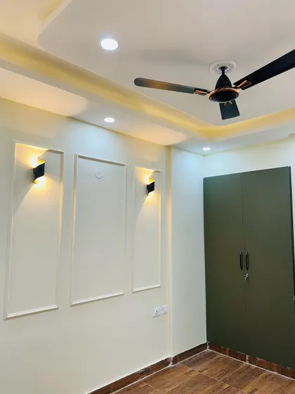 This bedroom features a simple POP moulding design on the wall with modern sconce lights, complementing the dark green wardrobe.