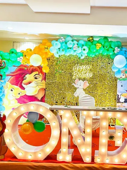 A classic jungle theme for a first birthday. The stage includes "ONE" marquee letters, a gold shimmer wall, and cutouts of various jungle animals like a lion and giraffe.