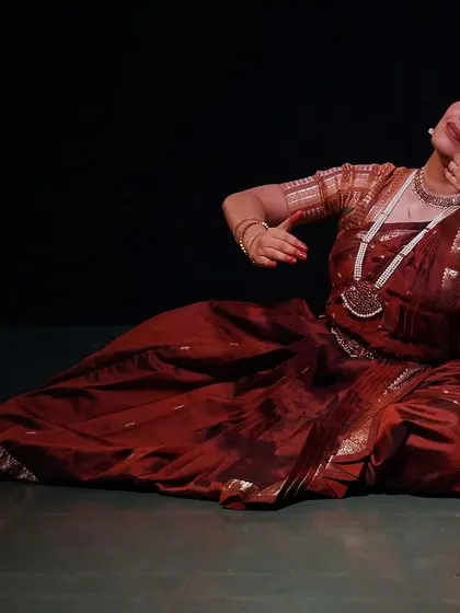 A graceful pose from 'Rasayatra', showcasing the dancer's control and artistry. The lighting highlights the rich colours of her costume against the dark backdrop.