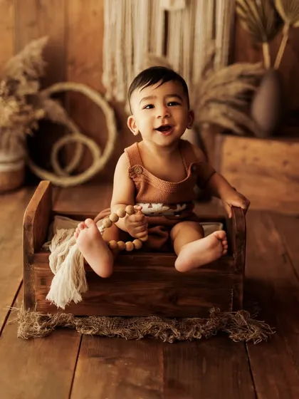 A heart-melting smile from a baby boy in a rustic wooden bed prop. The warm, earthy tones of the boho setup are perfect for sitter sessions.