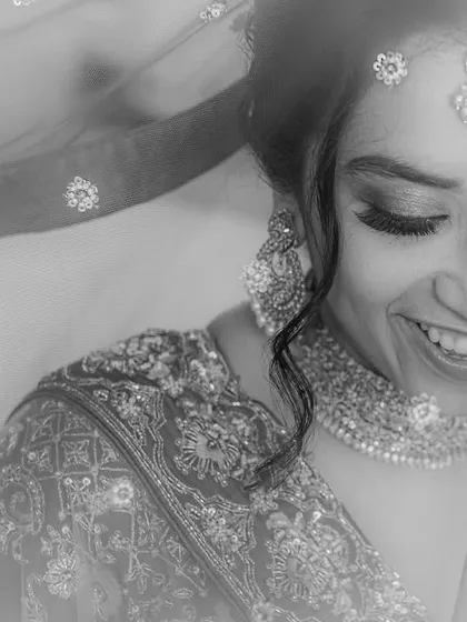 A beautiful black and white portrait of a bride, her face partially covered by a sparkling veil. Her joyful expression is the focus of this classic shot.