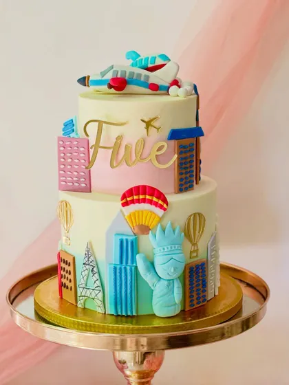 A travel-themed cake for a fifth birthday. This two-tiered design features landmarks from around the world, like the Eiffel Tower and the Statue of Liberty, plus a plane on top.
