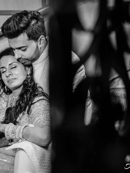 A quiet, intimate moment captured in black and white. The couple is sitting on a staircase, the groom's embrace is gentle and comforting.