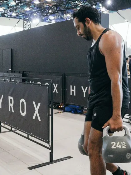 Farmer's carry with heavy kettlebells at a Hyrox event. This exercise is fantastic for building grip strength, core stability, and overall toughness.