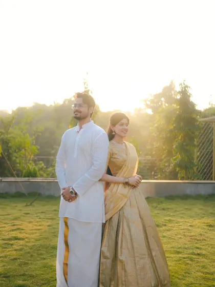 A couple in traditional South Indian attire stands back-to-back against a golden sunset. This pose is both playful and stylish, creating a beautiful pre-wedding portrait.