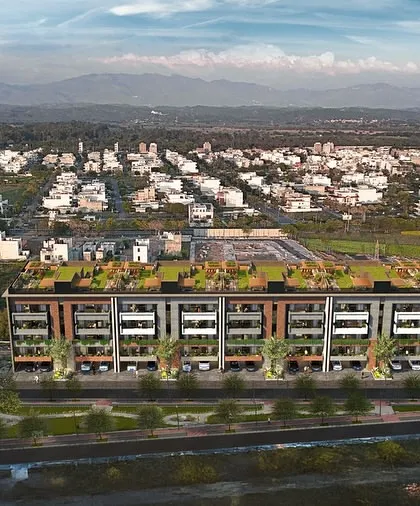 An aerial view of Gulnaar Lifestyle, showcasing its green rooftop and its placement within the larger cityscape, with mountains in the distance.