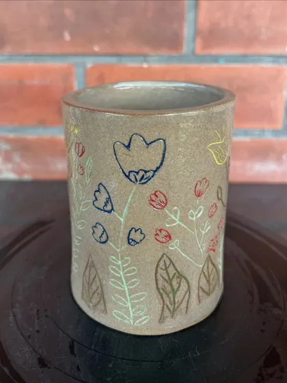 This charming tumbler was decorated by a student using colored underglazes to draw a delicate floral pattern before the final firing.