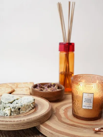 A stylish spread featuring our Bombay Orange Bourbon candle and reed diffuser. This fragrance, with notes of fresh orange, tangerine, and clove, is perfect for a sophisticated, cozy gathering.