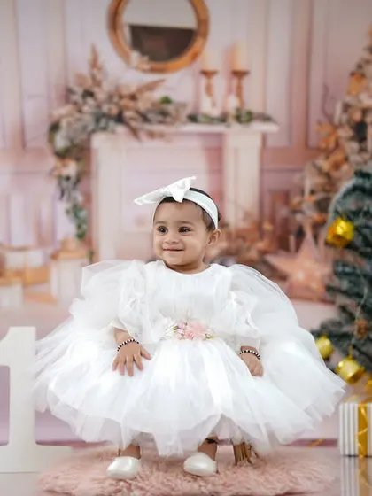 A beautiful, serene portrait of the little one in her fluffy white dress, surrounded by Christmas trees and presents.