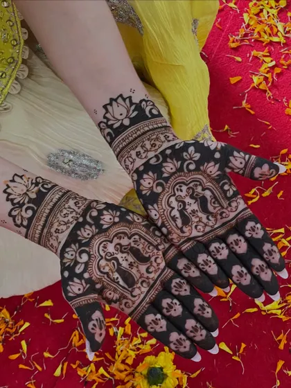 This design features bride and groom figures (dulha-dulhan) in the center of the palm, surrounded by floral patterns. The dark stain against the yellow and red background looks stunning.